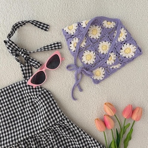 May include: A collection of summer accessories including a gingham dress, pink sunglasses, and a crocheted daisy bonnet. The bonnet is lavender with white and yellow flower details. A bouquet of pink tulips adds a pop of color.