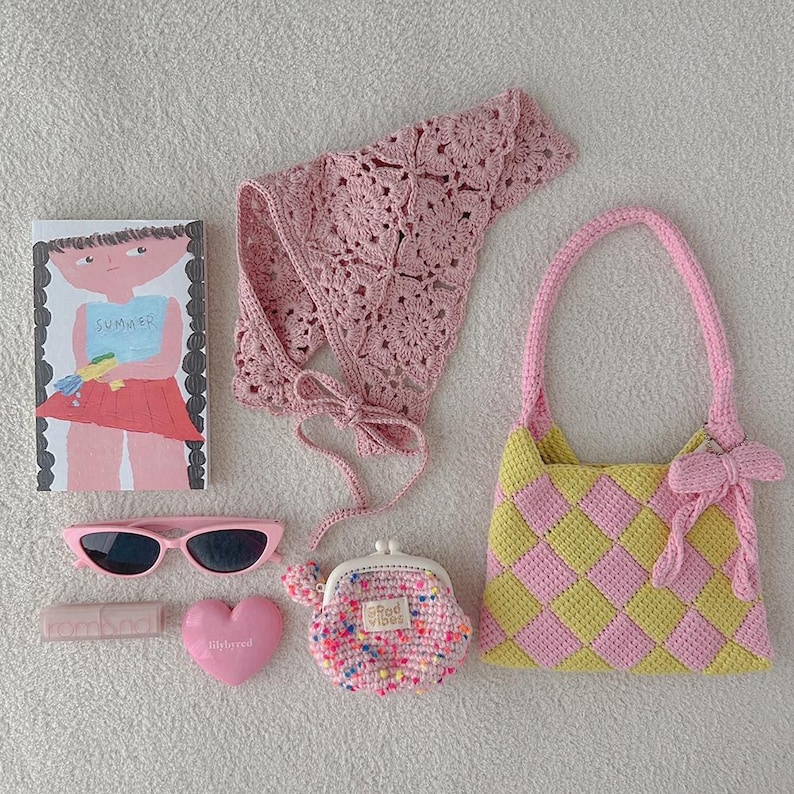 May include: A collection of pink accessories, including a crochet top, sunglasses, a heart-shaped item, a small coin purse, a lipstick tube, a book with a girl illustration, and a checkered handbag with a bow.