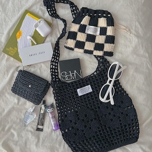 May include: A black crochet shoulder bag with a matching black and cream checkered drawstring pouch, a small black crochet wallet, white sunglasses, a NARS compact, a Bobbi Brown box, a book, wireless earbuds, and three small cosmetic items.