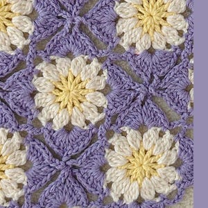 May include: Close-up of a crocheted floral pattern. The design features daisy-like flowers in white and yellow, surrounded by a lavender background. The crochet stitches create a textured, handmade appearance.