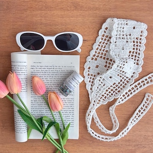 Puede incluir: Una composici&oacute;n plana con gafas de sol blancas, un libro, tulipanes rosas, una diadema de ganchillo blanca y un frasco de esmalte de u&ntilde;as. El frasco de esmalte de u&ntilde;as dice "Comet Puzz Nail Colour". Los art&iacute;culos est&aacute;n sobre una superficie de madera.