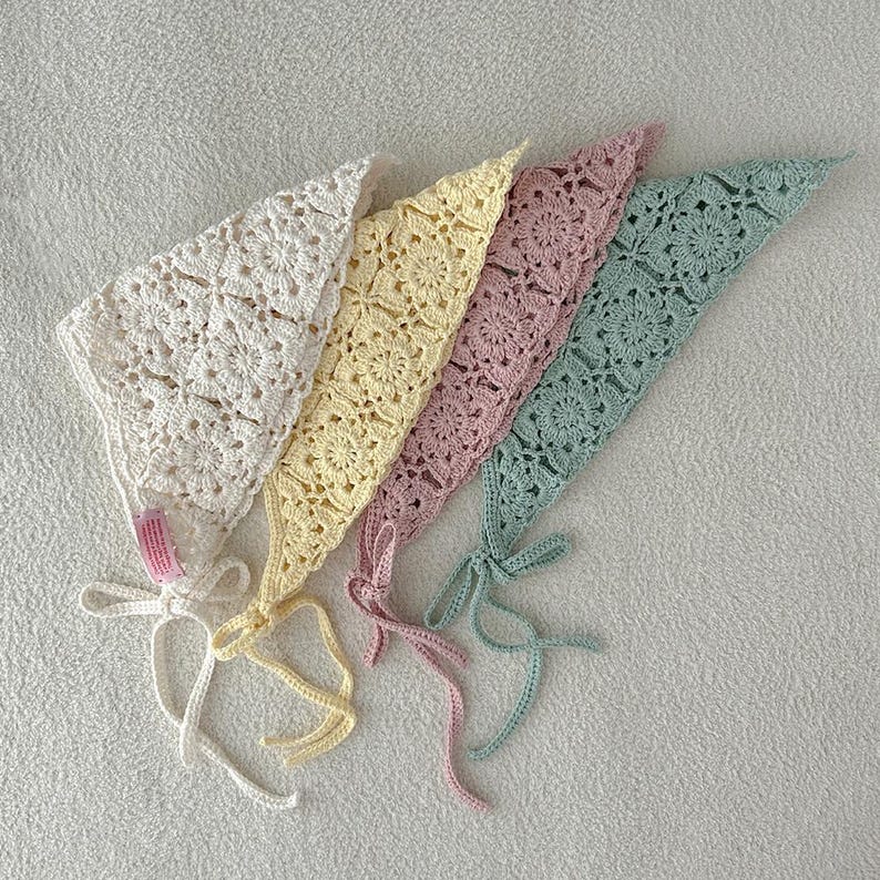 May include: Four handmade crochet bonnets in pastel colors: ivory, yellow, pink, and mint green. Each bonnet features a floral pattern and ties with matching ribbons. These bonnets are ideal for babies and young children.
