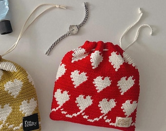 May include: Two crocheted drawstring bags with white heart patterns. One bag is red with the text "good vibes" and the other is yellow with the text "I'm crafty".