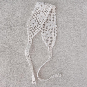 Puede incluir: Una diadema blanca de ganchillo de tejido abierto con un dise&ntilde;o delicado y calado. La diadema presenta una secci&oacute;n central rectangular con un patr&oacute;n repetido, que se estrecha en lazos largos y delgados. El art&iacute;culo se muestra sobre una superficie texturizada gris claro.