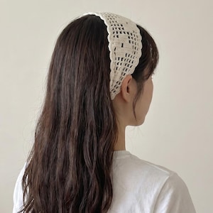 Puede incluir: Diadema de ganchillo color crema. La diadema est&aacute; hecha de un material tejido de tejido abierto. La diadema se lleva en la cabeza y es visible desde un lado, con cabello largo y casta&ntilde;o oscuro que fluye por la espalda. La persona lleva una camiseta blanca.