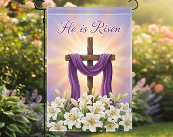 May include: A garden flag with the text "He is Risen" in script. The flag features a wooden cross draped with purple fabric, set against a radiant background. White lilies are at the base of the cross, with a garden setting.