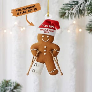 May include: A gingerbread man Christmas ornament with a red Santa hat and crutches. The hat has the text "YOUR NAME" and "WHAT A YEAR 2025". The ornament is flat, not 3D, and has a white cast on one leg.