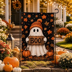 A Halloween-themed garden decoration featuring a ghost holding a sign that says "BOO!" surrounded by pumpkins, flowers, and a wreath.