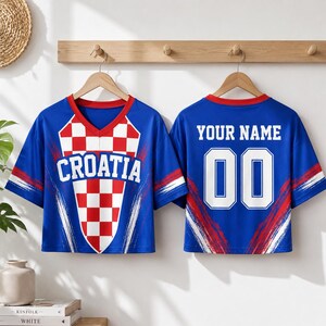 two blue and red Croatia soccer jerseys hanging on a wooden hanger. The jerseys have the word "Croatia" printed on the front and the number "00" on the back.