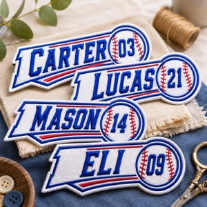 May include: Four white embroidered patches with blue borders and red accents, each featuring a name and a baseball graphic with a number. The names are Carter with 03, Lucas with 21, Mason with 14, and Eli with 09, all in blue lettering.