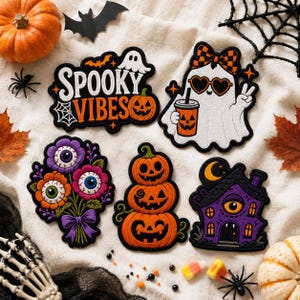May include: Five embroidered patches featuring Halloween themes: a sign reading Spooky Vibes, a ghost with heart-shaped sunglasses holding a pumpkin cup, a bouquet of eyeball flowers, a stack of three jack-o'-lanterns, and a purple haunted house.