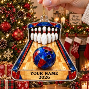 May include: A decorative bowling-themed ornament featuring a stained-glass style design with a blue and red bowling ball, white pins on a wooden lane, and a gold hanging loop. The bottom section includes the text YOUR NAME and 2026.