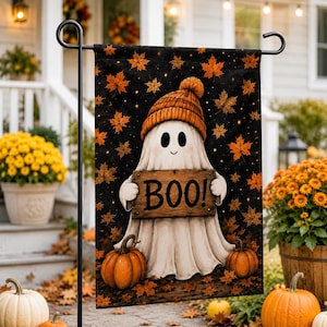 A Halloween-themed banner featuring a ghost holding a sign that says "BOO!" is displayed on a black pole, surrounded by pumpkins, flowers, and autumn leaves.