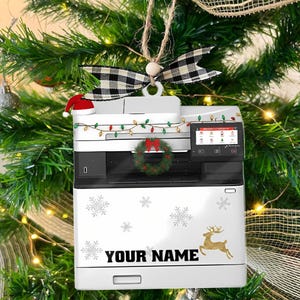 May include: A white Christmas ornament shaped like a printer, decorated with snowflakes and a gold reindeer. It has a small Santa hat, a wreath, and string lights. The text "YOUR NAME" is printed on the front.