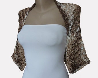 Könnte beinhalten: Ein braun-weißer Shrug mit offenem Gewebe und kurzen Ärmeln. Das Oberteil im Bolero-Stil wird auf einer Schaufensterpuppe präsentiert und zeigt sein strukturiertes, offenes Design. Das Kleidungsstück ist neutral gefärbt und zum Überziehen geeignet.