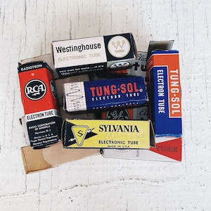 May include: A collection of vintage electronic tubes in their original boxes. The boxes are various colors, including red, blue, yellow, and white. The boxes have text that reads "Radiotron", "RCA", "Westinghouse", "Tung-Sol", and "Sylvania".