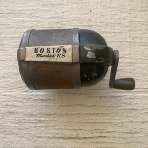 Puede incluir: Sacapuntas vintage de metal con mango verde. El sacapuntas tiene una etiqueta que dice "BOSTON Model KS".