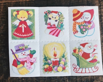 Könnte beinhalten: Eine Bogen mit Vintage-Weihnachtsaufklebern mit verschiedenen weihnachtlichen Motiven, darunter ein Engelmädchen, ein Strumpf, ein Schneemann, eine Kerze, ein Schneemannpaar und der Weihnachtsmann im Schlitten.