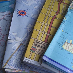 Può includere: Un mucchio di mappe vintage, tra cui una mappa di Creta, una mappa di una città con un sistema di trasporto pubblico e una mappa di un'area costiera con un logo 76. Le mappe sono in varie tonalità di blu, giallo e rosso.