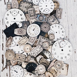 Może przedstawiać: Kolekcja vintage tarcz zegarowych w różnych rozmiarach i stylach, z oznaczeniami cyfr rzymskimi i arabskimi. Tarcze zegarowe są głównie białe z czarnymi oznaczeniami, a niektóre mają złoty odcień. Tarcze zegarowe są ułożone w przypadkowy wzór na białym drewnianym tle.