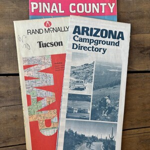 May include: Three vintage travel guides for Arizona. The top guide is pink and says "Amazing Pinal County". The middle guide is red and says "Rand McNally Tucson" with a map of Tucson. The bottom guide is white and says "Arizona Campground Directory" with photos of the Arizona landscape.