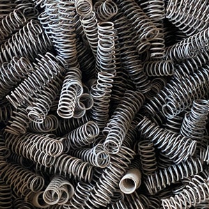 May include: A close-up image of a pile of silver metal springs. The springs are tightly coiled and arranged in a random pattern.