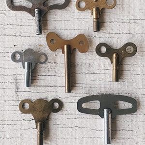 Könnte beinhalten: Eine Sammlung von sieben antiken Uhren-Aufziehschlüsseln. Die Schlüssel sind aus Metall und haben unterschiedliche Formen und Größen. Einige der Schlüssel sind aus Messing, andere aus Silber.