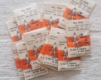 May include: A collection of vintage watch spring packs, each with a different size and strength. The packs are labeled with the brand name "AMSON" and the text "A coil of strength in your watch, made in Switzerland".