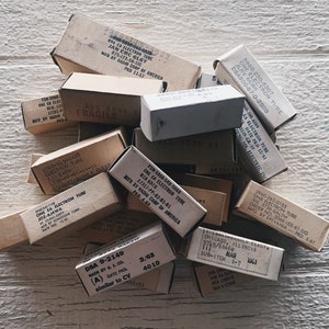 Puede incluir: Una pila de cajas de cartón vintage que contienen tubos de electrones. Las cajas están etiquetadas con el tipo de tubo, el fabricante y la fecha de producción. Algunas de las cajas están etiquetadas como "Frágil".