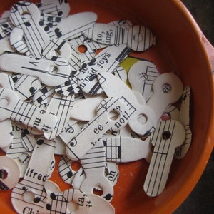 May include: A collection of small, white paper cutouts shaped like keys, filled with musical notation. The keys are inside an orange bowl. Some of the paper has text printed on it, including the words "Ifred" and "ce? not!"