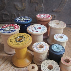 Puede incluir: Una colección de carretes de hilo vintage de madera en varios colores y tamaños. Los carretes tienen etiquetas con texto como "Coats & Clark's", "Mercerized", "Glace Finish" y "Pure Silk".