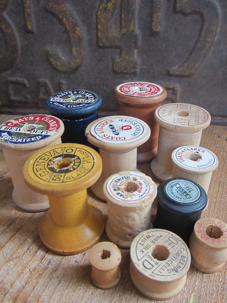 May include: A collection of vintage wooden spools of thread in various colors and sizes. The spools have labels with text such as "Coats & Clark's", "Mercerized", "Glace Finish", and "Pure Silk".