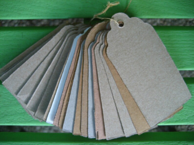 Puede incluir: Un conjunto de etiquetas de regalo de papel marr&oacute;n, beige y gris con un agujero perforado en la parte superior. Las etiquetas est&aacute;n dispuestas en forma de abanico.