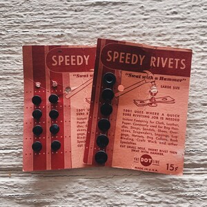May include: Two red and white cards with black rivets. The cards are labeled "Speedy Rivets" and "Speedy" with the text "Swat with a Hammer" on the larger card. The cards are for use with a hammer to attach rivets to fabric, leather, paper, and other materials.