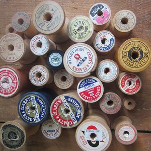 May include: A collection of vintage wooden thread spools with colorful labels. The spools are various sizes and feature different brands and thread types, including Coats & Clark's, Geneva, and Talon.