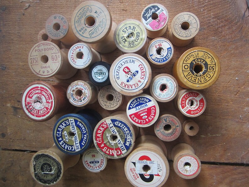 May include: A collection of vintage wooden thread spools with colorful labels. The spools are various sizes and feature different brands and thread types, including Coats & Clark's, Geneva, and Talon.