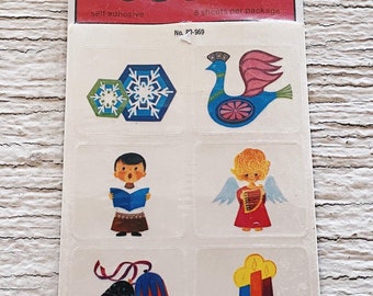 Könnte beinhalten: Eine Vintage-Packung mit selbstklebenden Dennison-Siegeln mit weihnachtlichen Illustrationen. Die Packung enthält 8 Blätter mit Aufklebern mit Bildern von einem Schneeflocke, einem Pfau, einem Weihnachtsliedsänger, einem Engel, Glocken und einer Kerze.