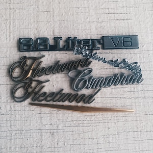May include: Close-up of a silver and gold car emblem with the text "2.8 Liter V6 Fleetwood Cimarron Fleetwood".