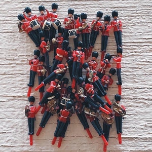 May include: A group of red and black toy soldiers in a marching band formation. The soldiers are playing various instruments, including drums, trumpets, and a tuba. The soldiers are arranged in a staggered formation, with the tallest soldiers in the back and the shortest soldiers in the front.