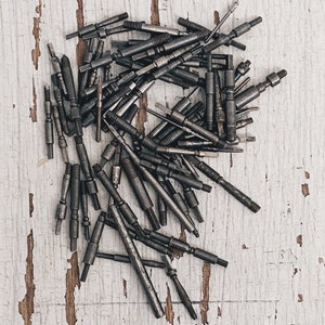 May include: A pile of assorted metal tools, including screwdrivers, drill bits, and other small tools, on a white wooden surface.