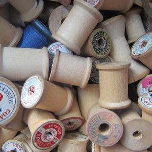 May include: A close-up of a pile of wooden spools of thread. The spools are various sizes and have different labels, including "J&P Coats", "Clark's", and "Mercerized".
