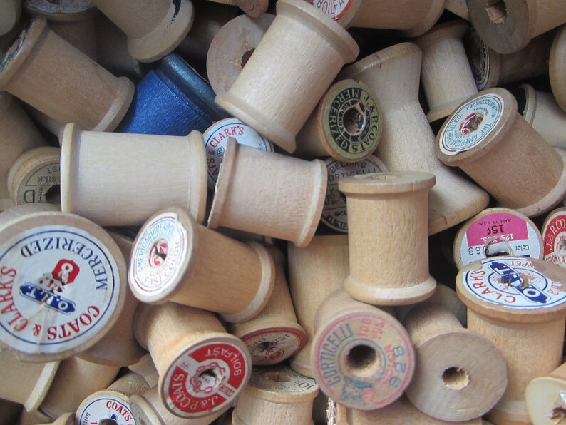 May include: A close-up of a pile of wooden spools of thread. The spools are various sizes and have different labels, including "J&P Coats", "Clark's", and "Mercerized".