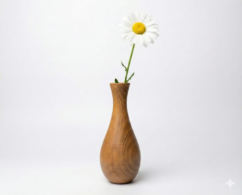 Puede incluir: Un jarr&oacute;n de madera con una sola margarita blanca. El jarr&oacute;n es de madera de color marr&oacute;n claro y tiene una forma suave y curvada. La margarita tiene un centro amarillo y p&eacute;talos blancos. El jarr&oacute;n mide unos 18 cm de altura.