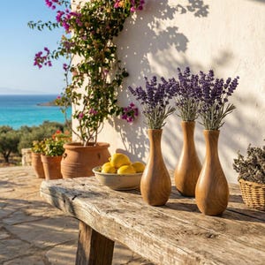 Puede incluir: Tres jarrones de madera con ramitas de lavanda sobre una mesa r&uacute;stica de madera. Un cuenco con limones y una cesta de mimbre con hierbas secas tambi&eacute;n est&aacute;n presentes. La escena se desarrolla al aire libre, con vistas al mar y una pared blanca con flores.