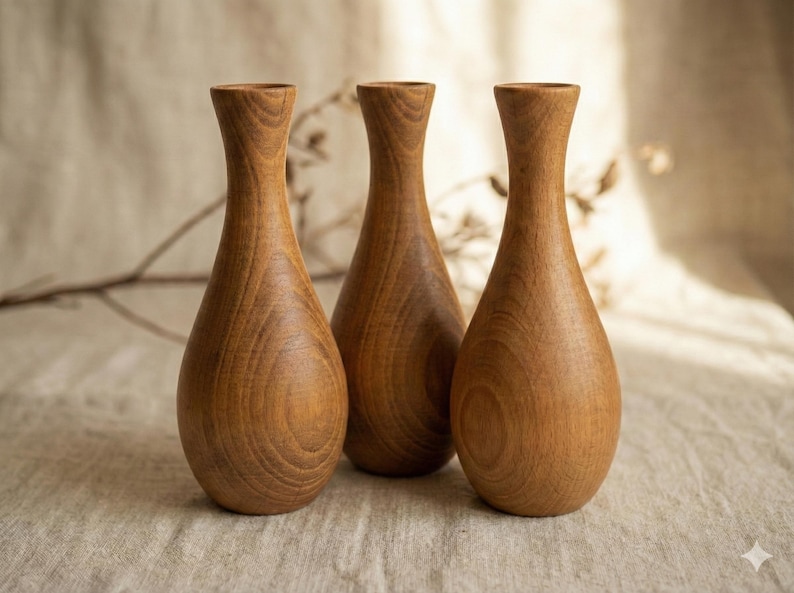 Puede incluir: Tres jarrones de madera con forma de l&aacute;grima y cuello estrecho. Los jarrones son de madera marr&oacute;n claro y tienen un patr&oacute;n de vetas naturales. Est&aacute;n dispuestos en fila sobre una superficie de color neutro.