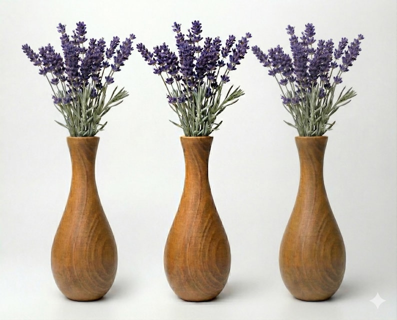 Puede incluir: Tres jarrones de madera, cada uno con un ramo de lavanda. Los jarrones son de color marr&oacute;n c&aacute;lido con un dise&ntilde;o liso y curvado. La lavanda tiene flores moradas y tallos verdes, creando un arreglo decorativo natural.