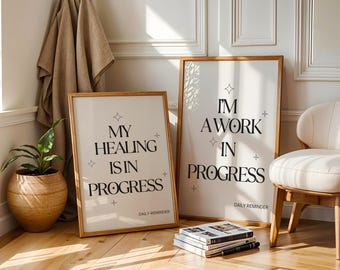 May include: Two framed art prints with inspirational quotes. One reads "My Healing Is In Progress" and the other says "I'm A Work In Progress." Both have a wooden frame and are displayed in a bright room with a chair and a plant.