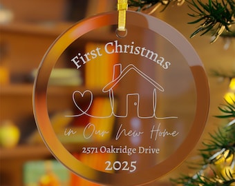 Pode incluir: Enfeite de Natal redondo em vidro transparente com fita dourada. O enfeite apresenta o texto "First Christmas in Our New Home" com um desenho de casa e coração, um endereço e o ano de 2025.