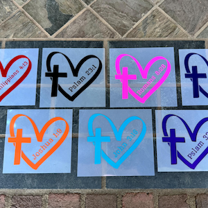 May include: A collection of heart-shaped decals, each featuring a cross and a Bible verse. The decals are in various colors, including red, black, pink, blue, orange, and purple. Verses include Philippians 4:13, Psalm 23:1, and others.