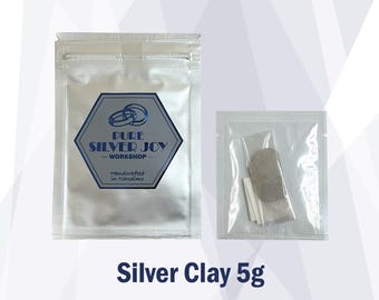 May include: Two silver clay packages. The larger package has a blue and silver logo that reads "Pure Silver Joy - Workshop - Handcrafted in Nanaimo." The smaller package contains silver clay and other items. The text "Silver Clay 5g" is below the packages.